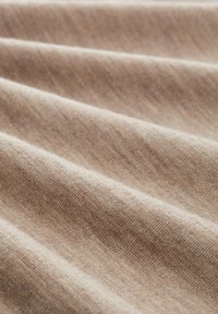 Hellbrauner Stoff mit weicher Textur, der sanfte Falten und ein dezentes Muster zeigt, welches die gewebte Struktur und die natürlichen Fasern betont.