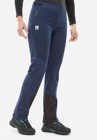 Pantalons de plein air navy avec une finition texturée, dotés d'un panneau noir sur le bas des jambes, de fermetures éclair sur les poches et d'un logo sur le devant.