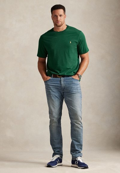 Πράσινο βαμβακερό κοντομάνικο μπλουζάκι, σε συνδυασμό με ανοιχτόχρωμο μπλε τζιν. Φορεμένο με μπλε και λευκά αθλητικά παπούτσια, με casual σχεδιασμό.