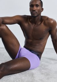 Lilla boxershorts med en svart Puma-logo i midjen, mykt stoff, tettsittende design og glatt tekstur, mot en lys bakgrunn.