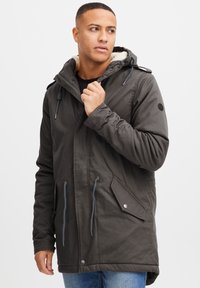 Parka en gris oscuro con capucha forrada de piel, cordones ajustables, bolsillos laterales y adornos de hardware plateado. Tejido de mezcla de algodón.