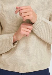 Bežový pletený sveter s textúrovaným rebrovaným vzorom, dlhé rukávy s priliehavými manžetami a rebrovaný pás.