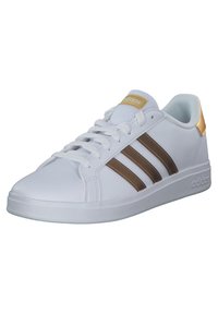 Białe buty sportowe z trzema brązowymi paskami i złotym akcentem na pięcie. Wykonane z gładkiej syntetycznej cholewki i teksturowanej podeszwy.