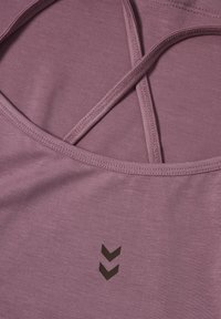 Débardeur violet avec un tissu texturé, des bretelles croisées dans le dos, et un petit logo sombre à chevrons à l'avant.