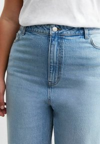 Jeans de tiro alto en azul claro, fabricados con denim, que cuentan con un cierre de botón en la parte delantera, un desvanecimiento sutil y un diseño clásico de cinco bolsillos.