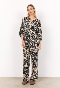 Tvådelad lounge set i beige med svart blommönster. Löst sittande blus med trekvartslånga ärmar, tillsammans med vida byxor. Mjuk textur.