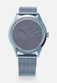 Montre à bracelet en maille argentée avec un cadran rond en gris, présentant un design en crocodile texturé et une lunette ornée de cristaux transparents.