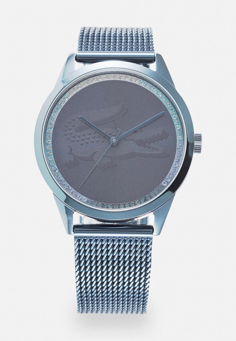 Montre à bracelet en maille argentée avec un cadran rond en gris, présentant un design en crocodile texturé et une lunette ornée de cristaux transparents.