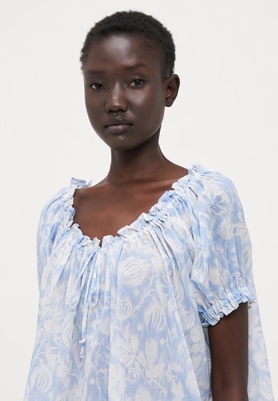 Light blue blouse made of soft fabric, featuring a floral pattern, gathered neckline, and short sleeves with elastic cuffs.