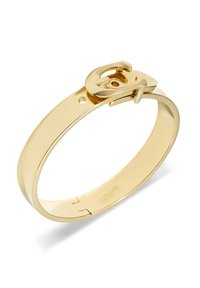 Zlatno metalno Coach narukvica s kopčom u obliku remena i ugraviranim imenom branda unutra.