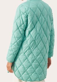 Gequilted lange jas in mintgroen, met diamanten patronen, een staande kraag en ribbelsmanchetten. Het materiaal lijkt lichtgewicht en glanzend te zijn.