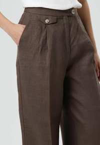 Bruine linnen broek met een hoge taille, geplooide voorkant, zijzakken en lichtgekleurde knoopaccenten. Glad oppervlak, wijde pijpen.