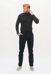 Schwarzer Rollkragenpullover kombiniert mit schwarzen Jogginghosen und hellgrauen Slippern. Einfaches Design mit einer figurschmeichelnden Silhouette.