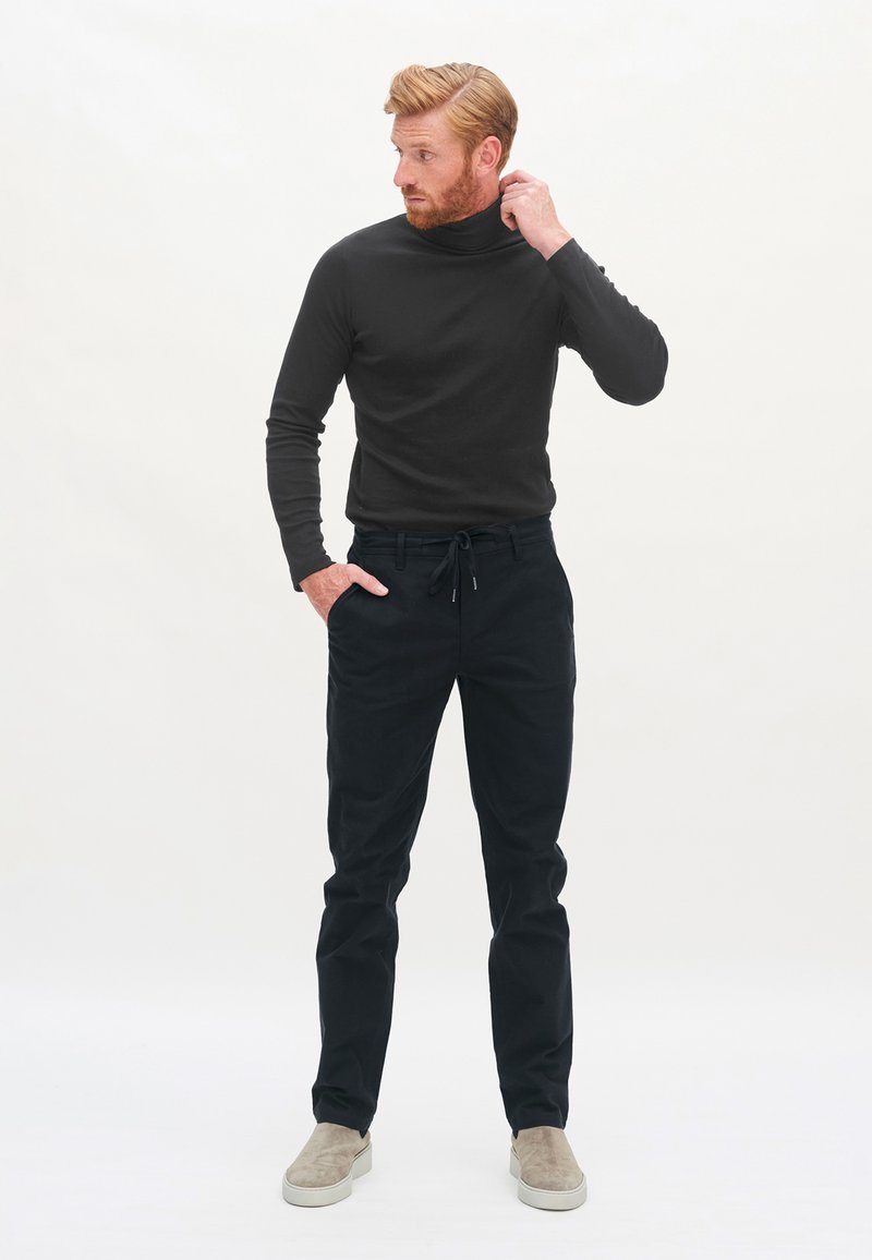 Schwarzer Rollkragenpullover kombiniert mit schwarzen Jogginghosen und hellgrauen Slippern. Einfaches Design mit einer figurschmeichelnden Silhouette.