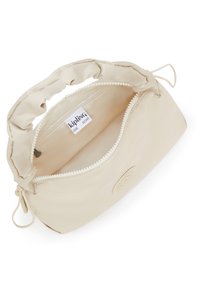 Beige Kipling-väska med rynkad handtag, öppen dragkedja som avslöjar ett tomt inre och varumärkesetikett i innerfickan.