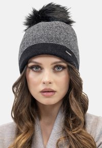Gorro de punto en gris con un pom-pom de pelo sintético negro. Presenta un patrón texturizado y una banda negra en contraste en la base.