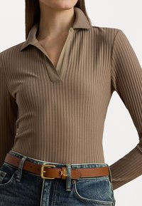 Polo ajustado de manga longa em tecido canelado marrom com colarinho em V. Usado com jeans azuis de cintura alta e um cinto de couro marrom com detalhes em dourado.