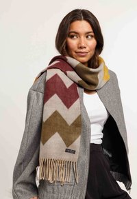 Cappotto in lana con un motivo a zig-zag nei colori bordeaux, oliva, beige e senape. Rifinito con bordi frangiati.