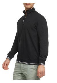 Svart genser med høy krage og glidelås, med hvite striper på mansjettene og sømmen, laget av et mykt, stretchy stoff.