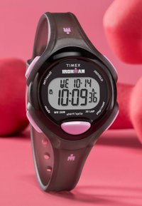 Digital Timex Ironman-klocka; svart plasthus med rosa detaljer, stor display som visar datum och tid, vattentålig upp till 50 meter.