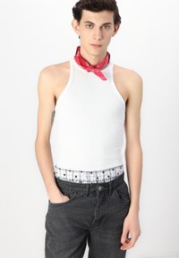 Top a coste bianco con collo alto, abbinato a jeans di denim neri con una vita a fantasia di stelle e un fazzoletto rosso attorno al collo.