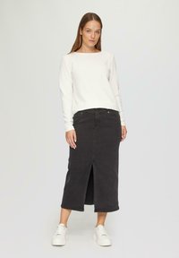 Haut long à manches blanches texturé avec un col bateau associé à une jupe en denim foncé avec une fente frontale, porté avec des baskets blanches.