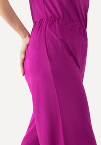 Pantaloni magenta con vita elastica e tasca laterale. Tessuto liscio e morbido con cintura aderente e gambe ampie, che evidenziano la silhouette.