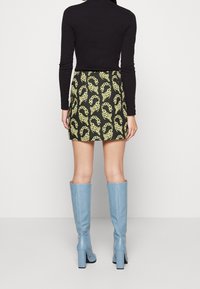 Haut noir à manches longues, mini-jupe à motifs avec chaînes jaunes sur fond noir, et bottes mi-mollet bleu clair texturées avec talons carrés.