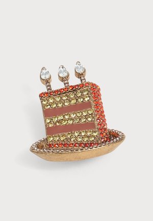 Épingle en forme de gâteau d'anniversaire à étages avec trois bougies allumées, décorée de strass rouges, jaunes et transparents sur une base dorée.