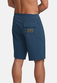Pantaloni da bagno blu da uomo con tasca posteriore, etichetta del marchio gialla, cuciture a contrasto, elastico in vita e design a gamba dritta.