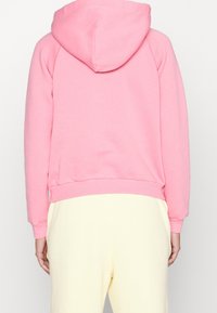 Rosa hoodie med snörning i huvan, ribbad mudd och nederkant, tillverkad av mjukt tyg, kombinerad med ljusgula sweatpants.