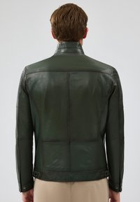 Giacca in pelle verde scuro con un design aderente, caratterizzata da un colletto alto e dettagli di cucitura orizzontale sulla schiena e sulle maniche.