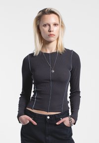 Maglietta nera a maniche lunghe con una texture a coste, caratterizzata da cuciture a contrasto di un blu chiaro e una silhouette aderente. Abbinata a jeans scuri.