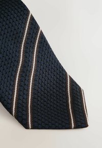 Marineblå struktureret slipse med et honningkage mønster og tre lodrette striber i brun og hvid. Triangulær spidsform.