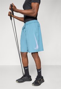 Light blue athletic shorts with an elastic waistband, a white striped logo, and side pockets. Worn with black athletic socks and shoes.
