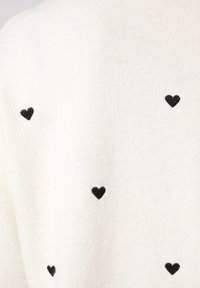 Witte stof met verspreide kleine zwarte hartpatronen, wat een textuur geeft en een zachte, gezellige uitstraling creëert.