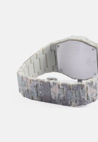 Digital klokke med et mønstret grått, hvitt og beige silikonarmbånd, med metallbakplate og rektangulære lenker i et vridd design.