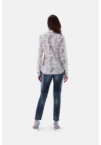 Bluse mit Blumenmuster und langen Ärmeln aus leichtem Stoff, mit Kragen und Knopfmanschetten. Kombiniert mit dunklen Jeans und blauen High Heels.