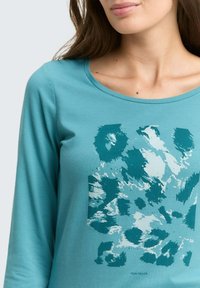 Türkises Langarm-T-Shirt aus weichem Stoff mit einem abstrakten Grafikdesign in verschiedenen Türkis- und Hellblautönen. Runder Halsausschnitt.