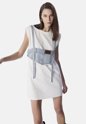 Abito bianco in cotone oversize con imbracatura in denim, spalline regolabili e patch con logo. Texture liscia, design casual.