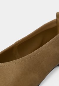 Gros plan sur le côté et la doublure intérieure d'une chaussure plate en daim beige avec des coutures propres et une texture lisse.