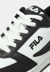 Αθλητικό παπούτσι FILA σε ασπρόμαυρο, με λευκά κορδόνια, δέρμα με υφή και λογότυπο στο πλάι και στη γλώσσα, εμφανιζόμενο σε κοντινή λεπτομέρεια.