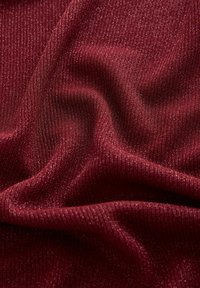 Bordo rebrasti materijal s teksturiranom površinom, koji sadrži suptilne metalik niti koje stvaraju blistavi efekt kroz tkaninu.