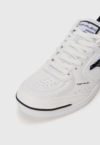Baskets en cuir blanc avec des perforations, lacets plats et un logo en accent noir. Caractéristiques d'une semelle texturée et d'un col rembourré.