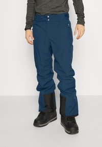 Blaue Outdoor-Hosen aus wasserabweisendem Material, ausgestattet mit einer Reißverschlusstasche, schwarzen Akzenten an den Knöcheln und einem verstellbaren Bund.