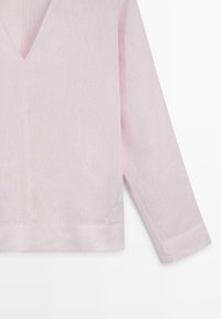 Lyserød langærmet top med subtil tekstur og V-formet udskæring, vist fra taljen til ærmets ende.