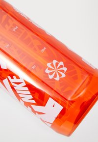 Orange plastvandflaske med hvide accenter, med måleenheder i milliliter og ounces, samt et cirkulært blomstermotiv.
