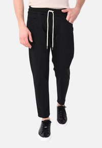 Pantaloni jogger neri con cintura elastica, cordoncino regolabile, tasche laterali e vestibilità affusolata; indossati con sneaker nere.