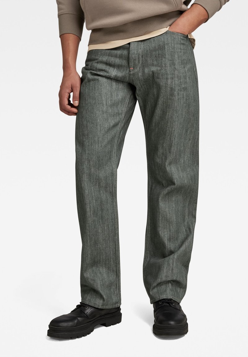 Donkergroene denim broek met een recht model, voorzien van lichte stiksels, zijzakken en gecombineerd met zwarte veterschoenen.