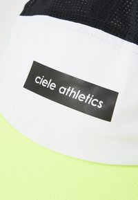 Laufen Kappe mit einem Schwarz-Weiß-Design, einer strukturierten Oberseite und einem leuchtend gelben unteren Teil, beschriftet mit "ciele athletics."